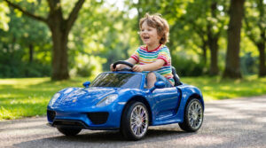 Jeune garçon blond rieur au volant d'une voiture électrique Kiddi Quad bleue, sur un chemin ensoleillé, entouré d'arbres.