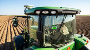 Vue d'un tracteur John Deere vert équipé RTK, conduit par un agriculteur dans un champ avec des rangs parallèles. Un écran affiche la navigation de précision.